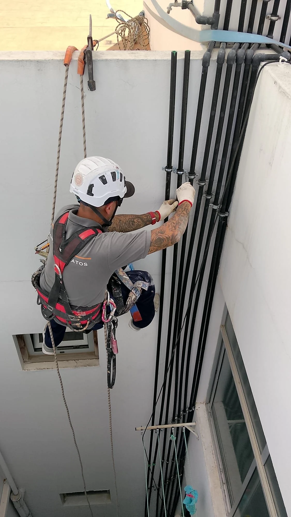 Operario de Matos Fontanería descolgado con arnés instalando bajantes en una fachada de Las Palmas