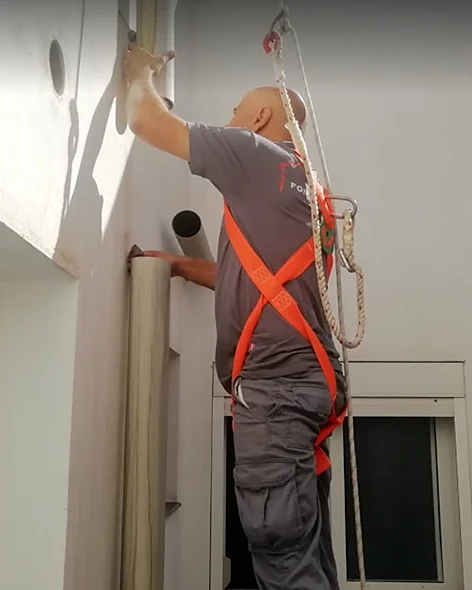 Operario con arnés instalando un bajante en la fachada